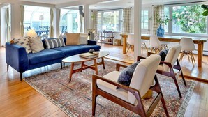 A spacious living room with a blue sofa, white armchairs, a coffee table, and a dining area with a table and chairs.