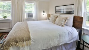 A bedroom with a large bed, a bedside table, a lamp, and a window with curtains.