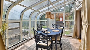 A greenhouse with a table and chairs, large windows, and a hanging light fixture.