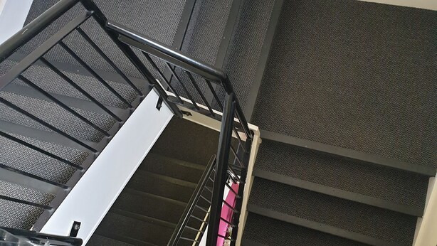 Eine Treppe mit Metallgeländer und strukturierter Stufenfläche.