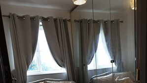 Ein Schlafzimmer mit zwei Betten, jeweils mit Kopfteil, und einem großen Fenster mit Vorhängen.
