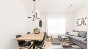 Een moderne woonkamer met een grijze bank, een houten eettafel met zwarte stoelen, een zwart-wit gestreepte vloerkleed en een zwarte kroonluchter.