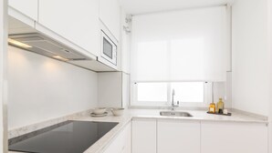 Een moderne keuken met witte kasten, een zwarte inductiekookplaat, een roestvrijstalen spoelbak en een raam voor natuurlijk licht.