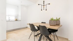 Een moderne keuken met witte kasten, een houten eettafel, zwarte stoelen en een opvallende zwarte hanglamp.
