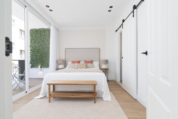 A bedroom with a large bed, bedside tables, a bench, and a sliding door.