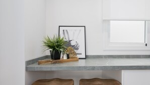 A kitchen counter with a framed picture, a potted plant, and two wooden stools.