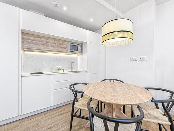 Une cuisine moderne avec des meubles blancs, un plan de travail en bois, un four à micro-ondes encastré et une table de salle à manger ronde, accompagnée de quatre chaises.