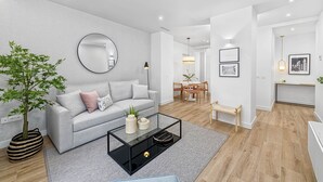 A modern living room with a grey sofa, a round mirror, a coffee table, and a dining area with a bench.