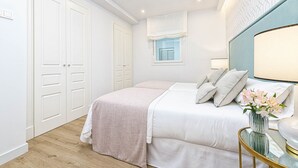 A bedroom with a double bed, bedside tables, a window with curtains, a wall-mounted lamp, and a decorative vase.