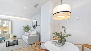 A modern living room with a glass coffee table, a round dining table with chairs, a sofa, and a large pendant light.
