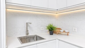 A modern kitchen with white cabinetry, a stainless steel sink, and a potted plant on the countertop.