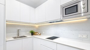 A modern kitchen with white cabinets, a stainless steel microwave, a sink, and a built-in oven.