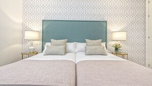 Una cama doble con cabecera color turquesa, dos mesitas de noche con lámparas y un papel tapiz estampado.