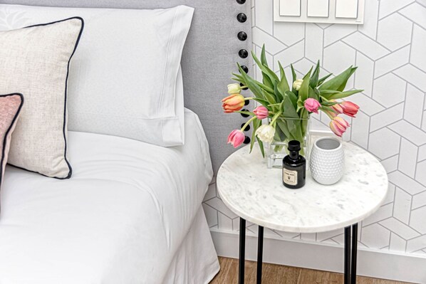 A neatly arranged bedroom with a bed, a small round table with a vase of flowers, and a wall with a geometric pattern.