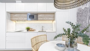 Una cocina moderna con armarios blancos, un microondas y un comedor con una mesa y sillas blancas.