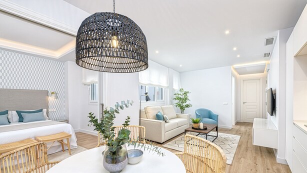 Una sala de estar moderna con una mesa de comedor redonda, muebles de mimbre y una lámpara colgante negra grande.