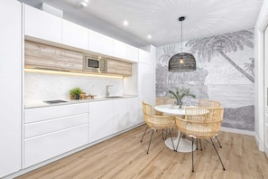 Une cuisine moderne avec des meubles blancs, un plan de travail en bois et un coin repas agrémenté de chaises en osier et d’une table ronde.