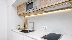A modern kitchen with white cabinetry, a stainless steel sink, a built-in microwave, and an induction cooktop.