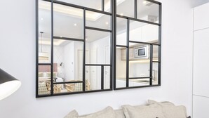 A modern living room with a large mirror, a sofa with cushions, and a television in the background.