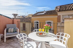 Una terraza con una mesa redonda, sillas blancas, un sofá y una urna decorativa.