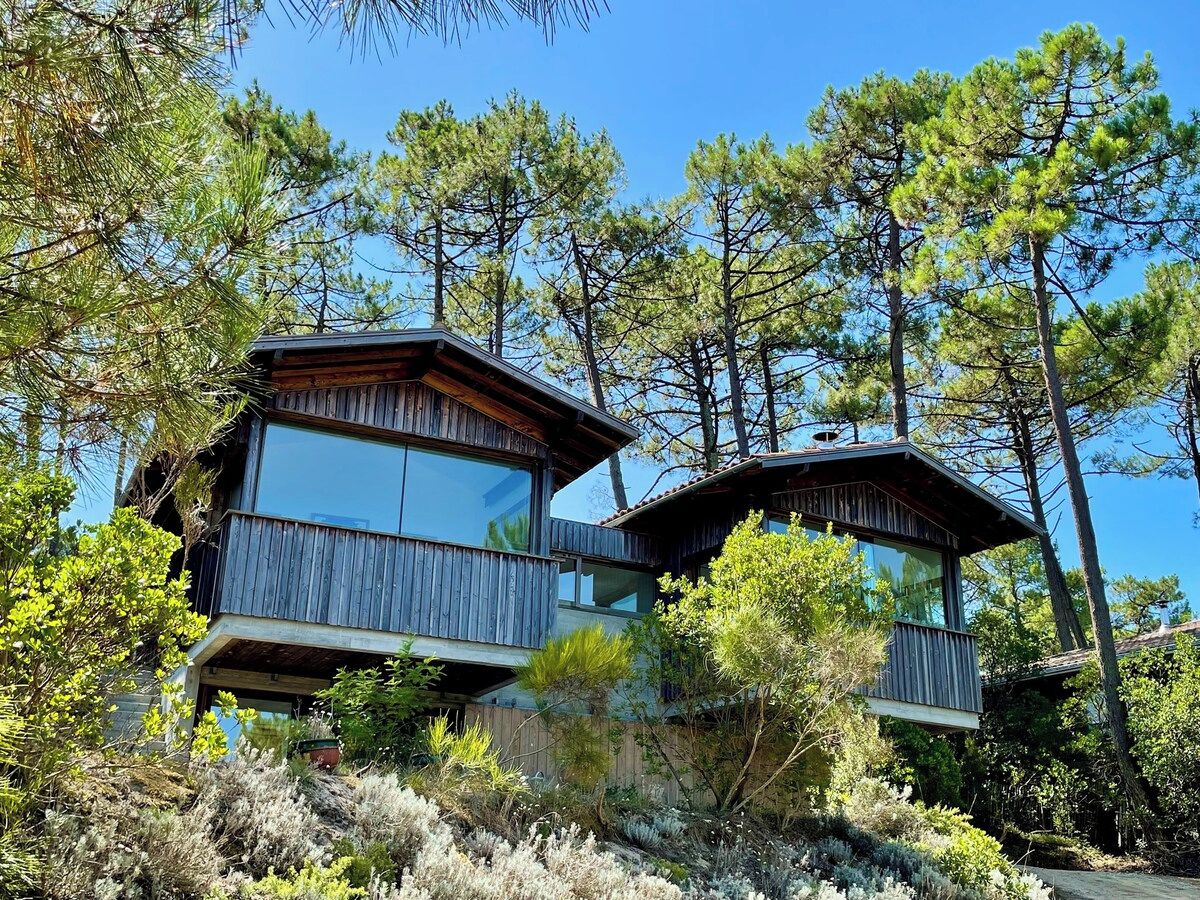 A two-story cabin with a balcony, surrounded by trees.