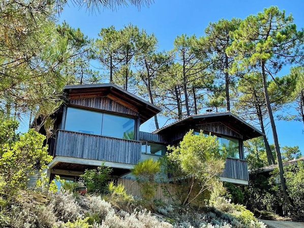 A two-story cabin with a balcony, surrounded by trees.