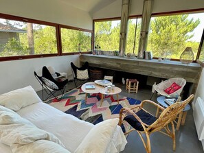 A cozy room with a bed, a round table, and two chairs. There is a fireplace and a view of trees outside. - Architect villa in nature near ocean & bay A0389 (Lège-Cap-Ferret)