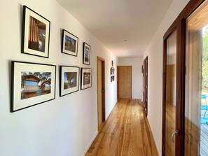 A hallway with wooden flooring, framed pictures on the walls, and a door leading to an outdoor area.
