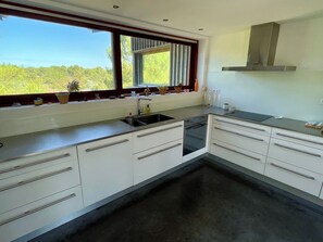 A modern kitchen with white cabinetry, a stainless steel sink, and a window with a view of greenery. - Architect villa in nature near ocean & bay A0389 (Lège-Cap-Ferret)