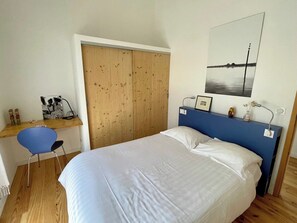 A bedroom with a single bed, a desk with a chair, a wooden wardrobe, and a framed picture on the wall.