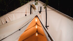 A tent with a bed inside, a hanging light, and a campfire. - Glamping | Outdoor Shower | Bathroom (Providence)
