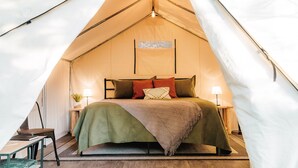 A tent with a bed, two bedside tables, and a lamp. - Glamping | Outdoor Shower | Bathroom (Providence)