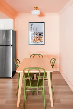 Uma área de refeições com mesa de madeira e cadeiras verdes, uma geladeira de aço inoxidável e um quadro na parede.