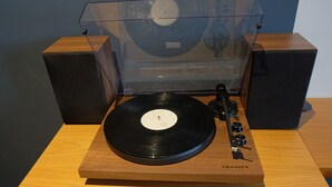 A turntable with a transparent cover, a record, and speakers on a wooden table. - Cosy and Stylish (T'bilisi)