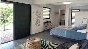 A modern bedroom with a bed, a small desk, a chair, and a large window. - Studio O'KALM - Le Gosier (LE GOSIER)