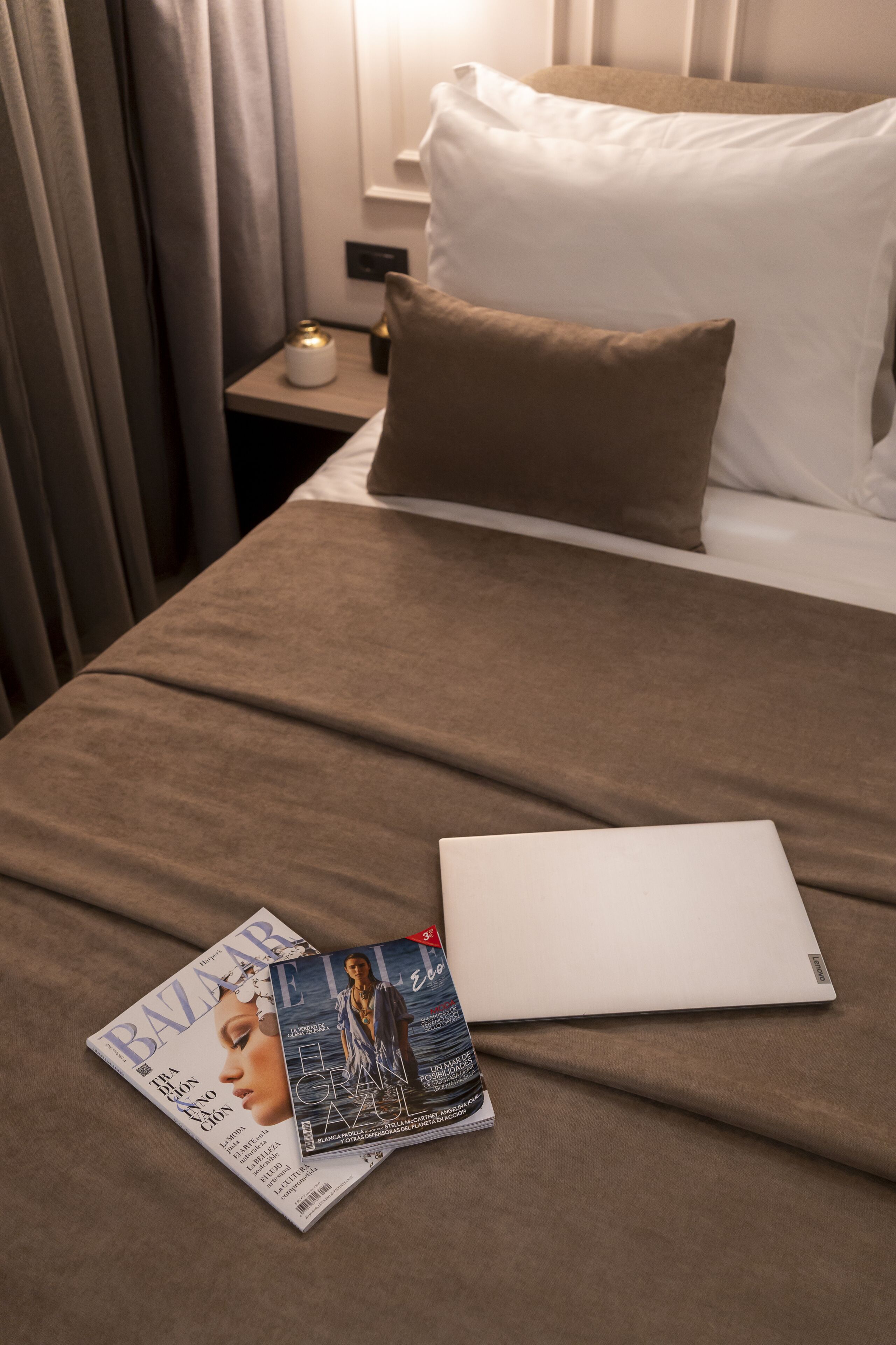 Un lit bien fait, avec une couverture marron, un oreiller blanc et un magazine posé sur le lit.
