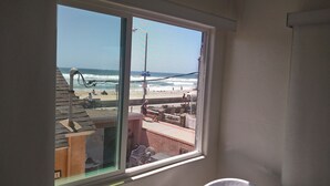 A beach view from a window, including a sandy beach, ocean waves, and a few people. - Studio #1 Fully-equipped with Boardwalk Patio Access - Oceanfront! Pet-Friendly! (San Diego)