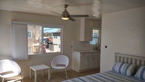A bedroom with a bed, a desk, a chair, a ceiling fan, a window, and a kitchenette. - Studio #1 Fully-equipped with Boardwalk Patio Access - Oceanfront! Pet-Friendly! (San Diego)