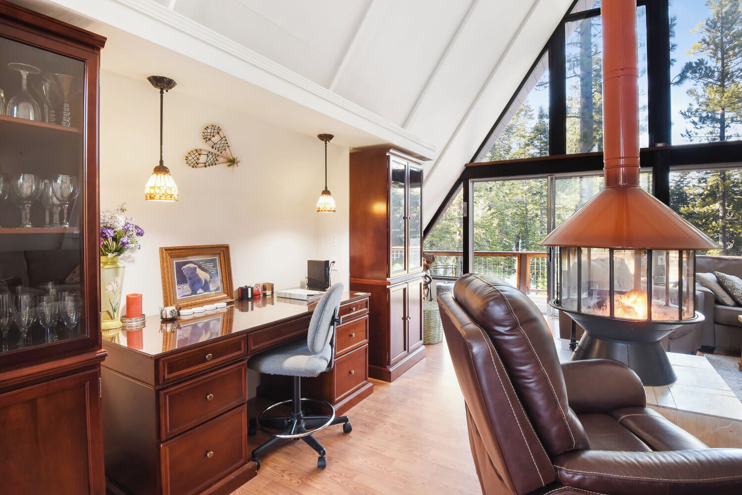 A spacious room with a wooden desk, leather chairs, and a large window offering a view of trees.