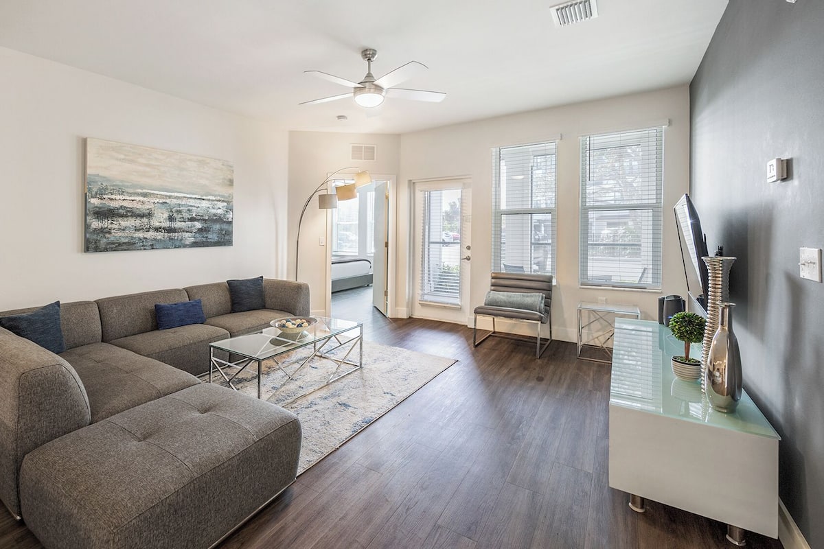 A modern living room with a sectional sofa, a glass coffee table, and a dining area with a bench.