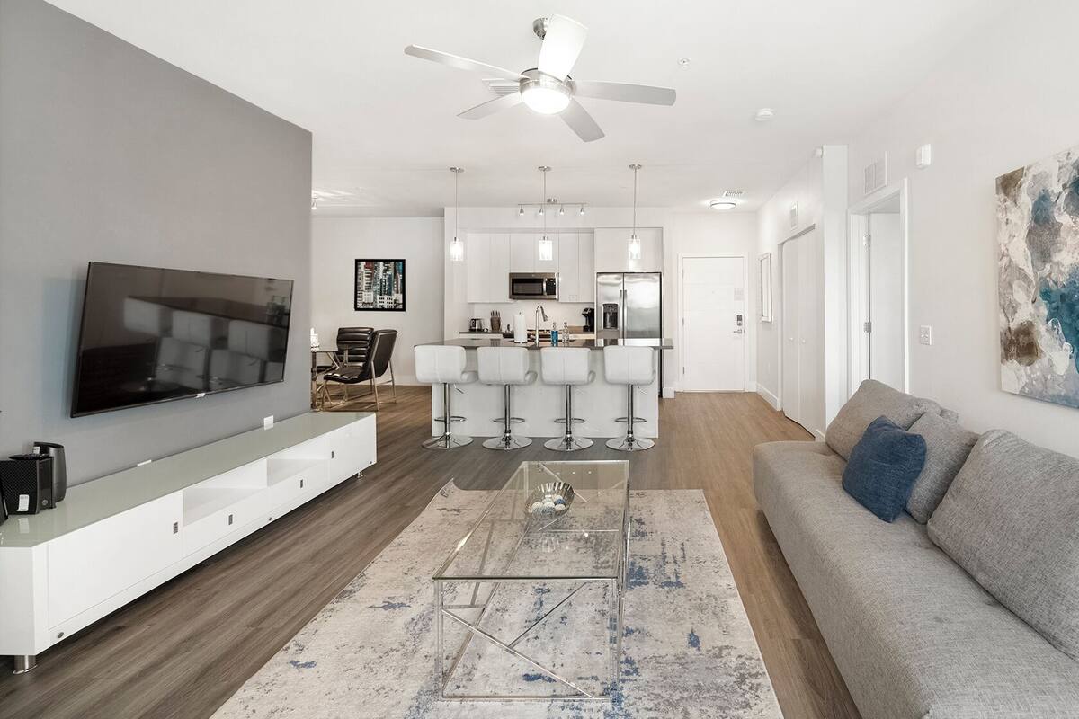 A modern living room with a flat-screen TV, a sofa, a coffee table, and a bar area with stools.