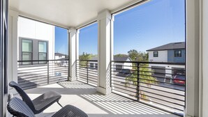 A balcony with two wicker chairs, large windows, and a view of a parking area and buildings. - Landing Tampa Westshore (Tampa)