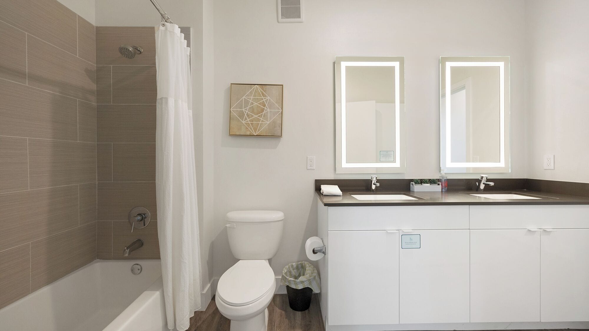 Een moderne badkamer met douche, toilet en wastafel met twee spiegels.