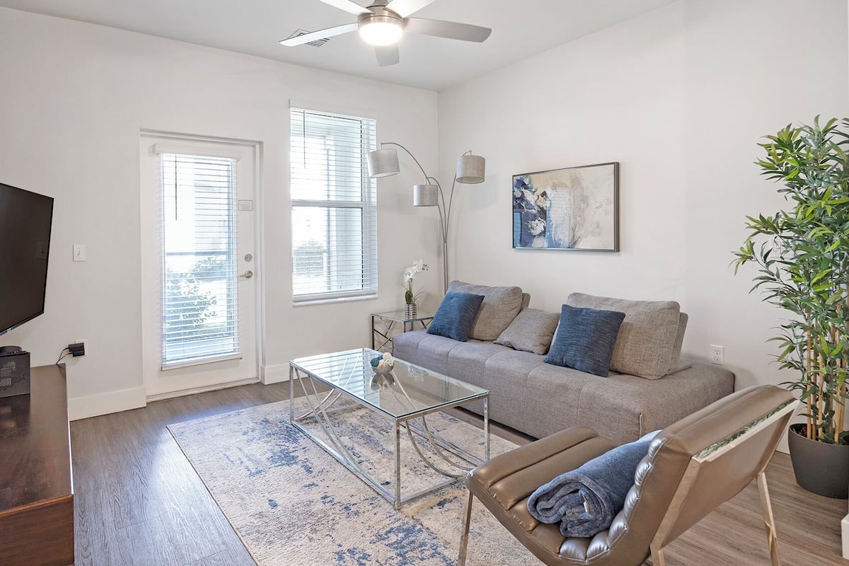 A living room with a sofa, a glass coffee table, a TV, and a ceiling fan.