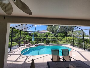 Et overdækket udendørsområde med swimmingpool, liggestole og et bord.