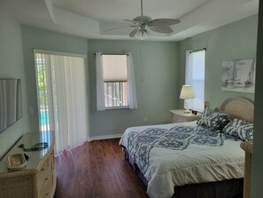 A bedroom with a bed, a nightstand, a lamp, a ceiling fan, and a window with curtains.