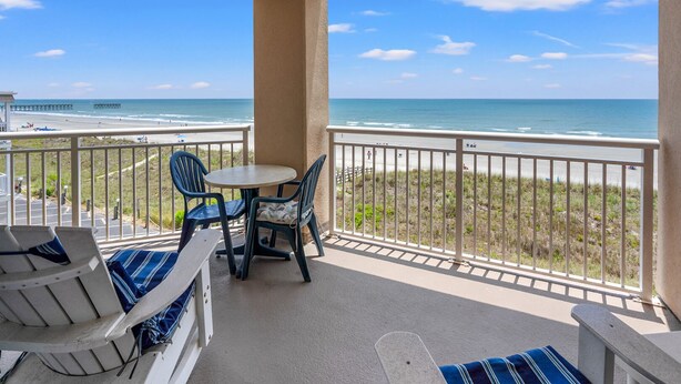 A balcony with a view of the beach and ocean, featuring a table and chairs, and a lounge area with a bench. - Escape to the ultimate beach retreat (North Myrtle Beach)