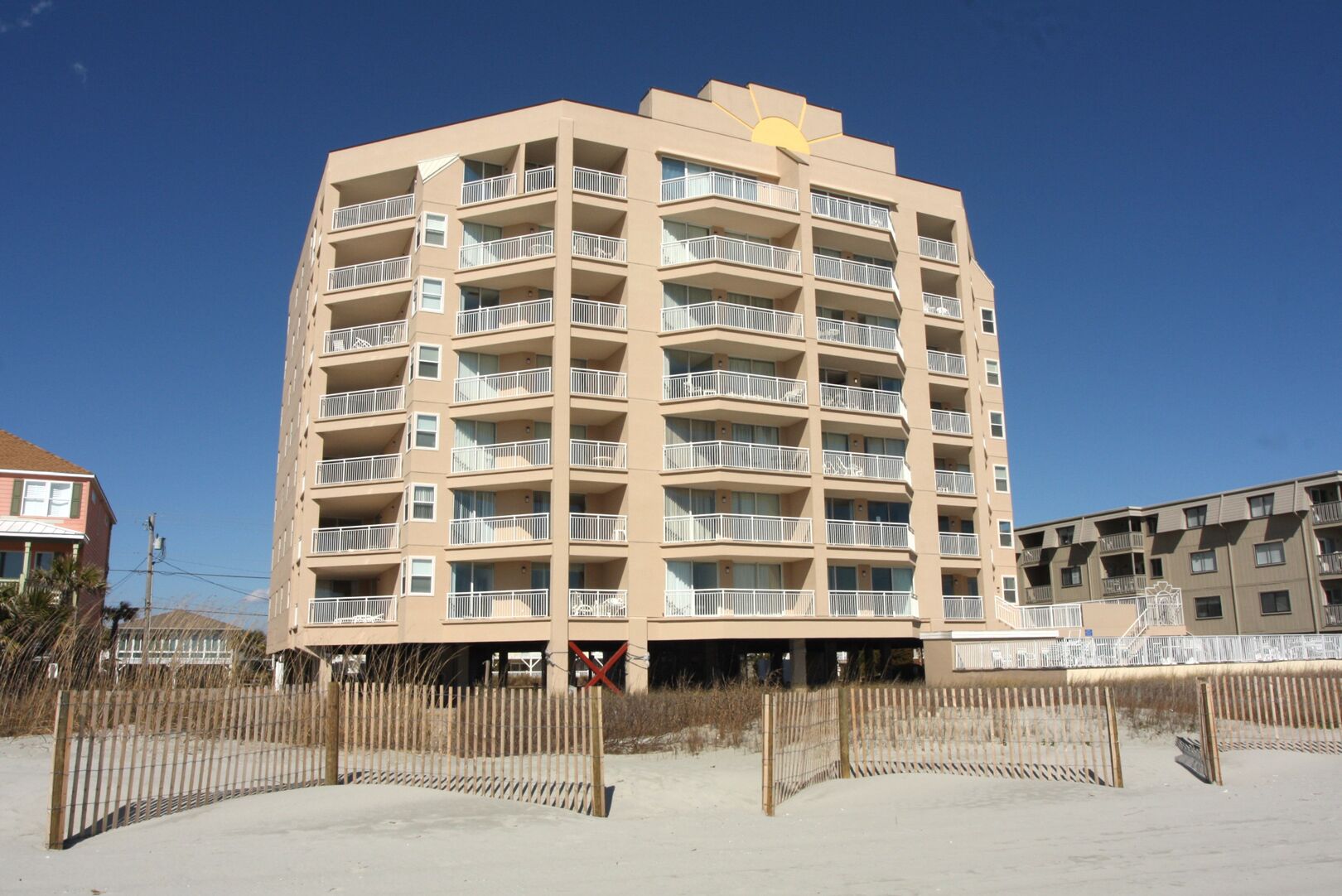 A multi-story hotel with balconies, a sandy beach in front, and a clear blue sky.