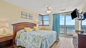 A bedroom with a wooden bed, a nightstand, a desk, a television, and a balcony with a view of the ocean. - Escape to the ultimate beach retreat (North Myrtle Beach)