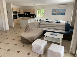 A compact living space with a kitchenette, a sofa, a covered ottoman, and a dining area.
